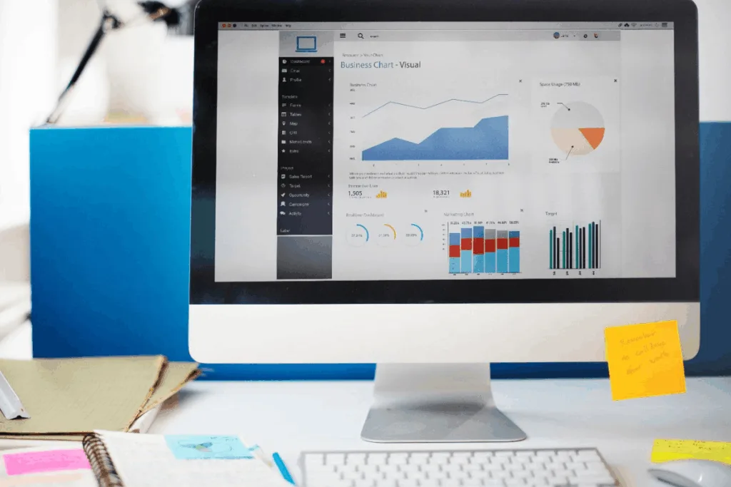 Computer screen displaying business charts, including line and pie graphs. A cluttered desk with notes and documents is visible, suggesting productivity.