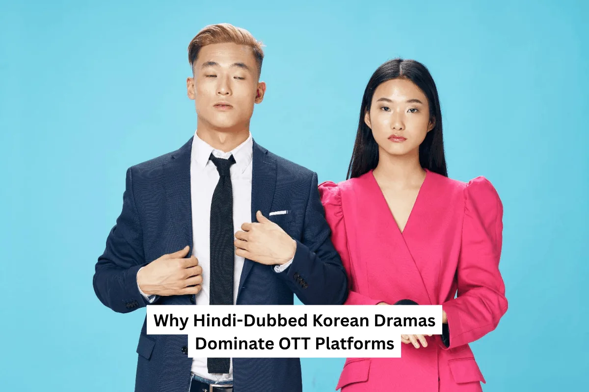 A man in a suit and a woman in a bright pink dress stand against a blue background. Text reads, "Why Hindi-Dubbed Korean Dramas Dominate OTT Platforms."